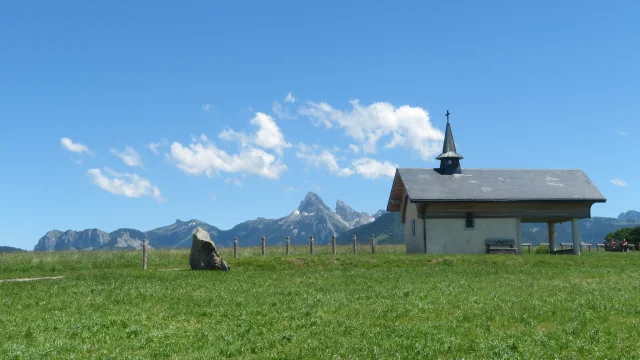Chapelle de Champeillant against a blue sky and green grass. The Dent d'Oche peak stands out in the background.
