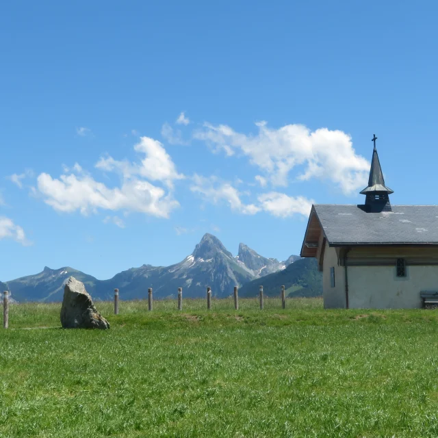 Chapelle de Champeillant against a blue sky and green grass. The Dent d'Oche peak stands out in the background.