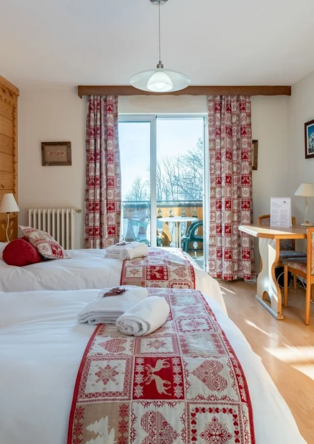 Hotel Le Bois Joli Saint Paul En Chablais. Lichte houten kamer met witte bedden en rode spreien die passen bij de gordijnen.