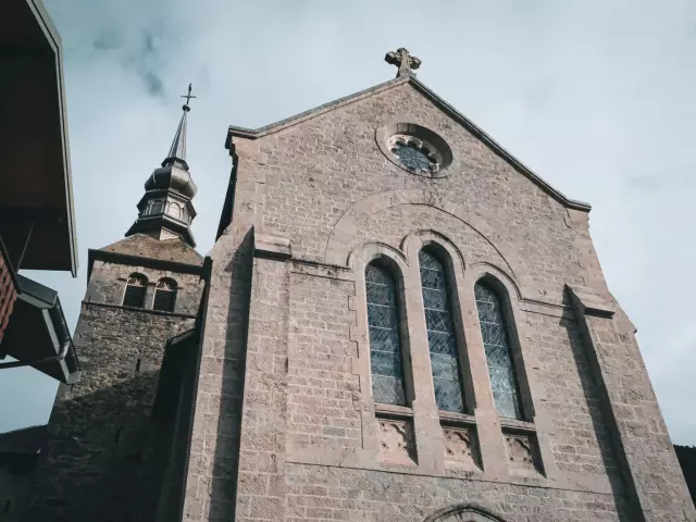 The Abbey of Abondance is located in the heart of the mountains. The photo shows the forecourt of the Abbey, with its huge grive stone façade and imposing stained-glass windows at the front.