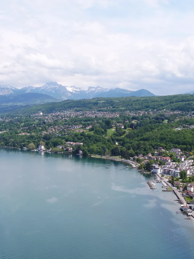Lake and coast in the foreground. Buildings and trees can be seen from a drone view with the mountains in the background.