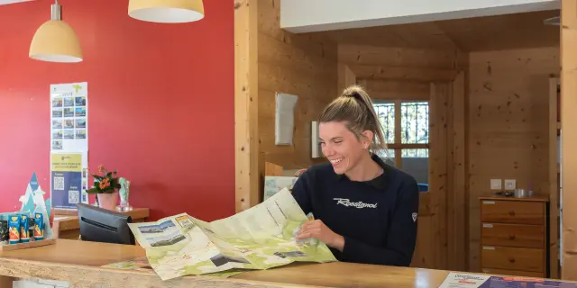 Conseillère de l’Office de Tourisme de Thollon, souriante, derrière le comptoir en bois, présentant une carte touristique.