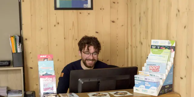 Conseiller de l’Office de Tourisme de Bernex, souriant, derrière le comptoir en bois.