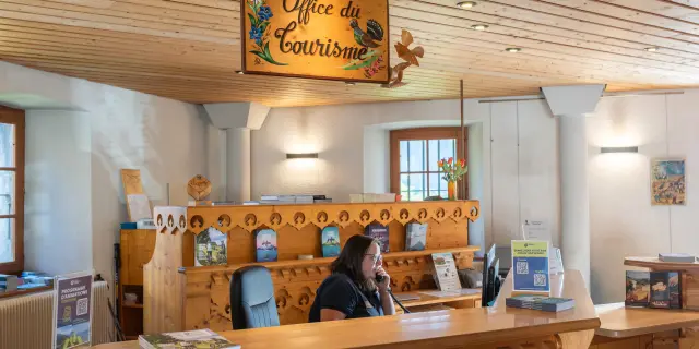 Conseillère de l’Office de Tourisme de Thollon, souriante, derrière le comptoir en bois, au téléphone.